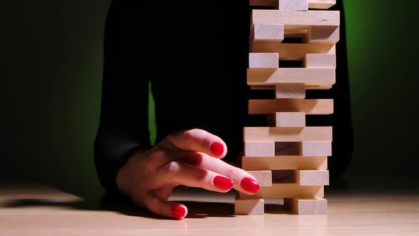 A Girl Plays the Jenga Board Game Sitting at a Table on a Green Gradient Background