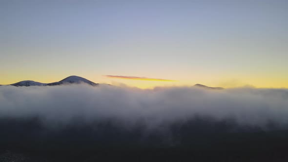 Aerial view of vibrant sunrise over white dense fog with distant dark peaks of Carpathian