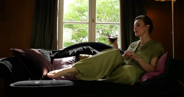 Woman with glass of wine sits down in sofa. Boudoir scene, slider shot
