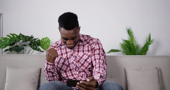Cheerful handsome african man lucky in game on smartphone