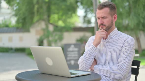 Middle Aged Man Thinking While Working on Laptop in Outdoor Cafe