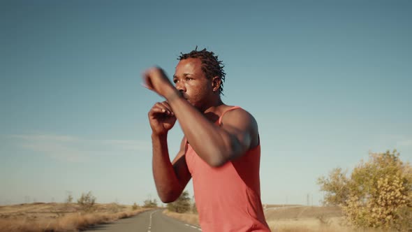 Black muscular man hits air practicing boxing punches, shadow fight, side view. African-American man