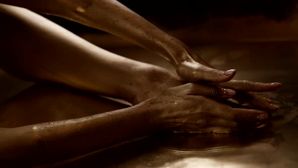 Female Body in Bronze Water Woman is Smearing Gold Paint Over Skin of Legs and Hands Closeup View