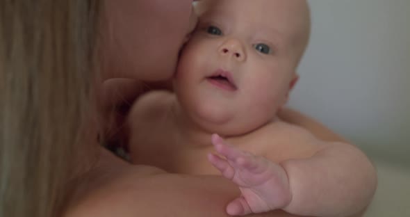 Happy Mother Holds a Little Baby Boy and Kisses Him on Background