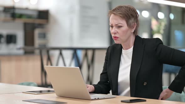 Old Businesswoman with Laptop Having Back Pain in Office 