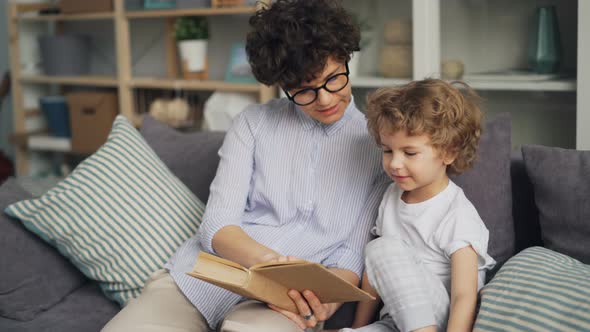 Cute Little Kid Reading Book with His Loving Mother and Smiling on Sofa