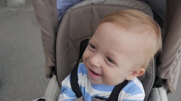 Little and Funny Boy Sitting in the Pram and Waiting for Mom