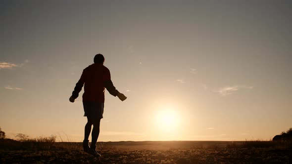 Man Boxer in Sportswear Trains Outdoors Jumping Rope Against Background of Sunset Back View