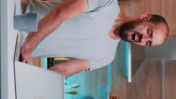 Vertical Video Exhausted Man Yawning Sitting in Kitchen at Laptop