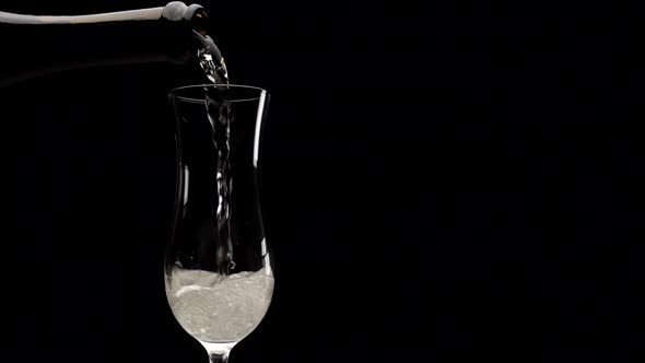 Pouring champagne on flute in black background. Sparkling white wine alcohol  drink splashing at slo