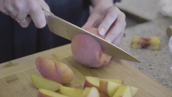 A woman chef is cutting peaches on a wooden board in the kitchen.