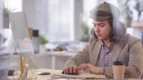 Man in Flat Cap and Jacket Working on Computer in Office