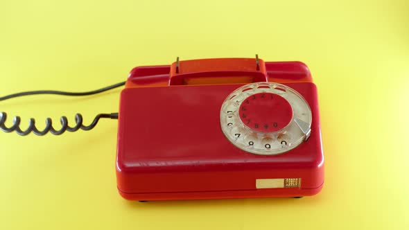 Hand Picks Up Red Landline Phone on Yellow Background