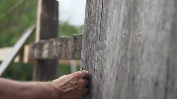 A Man Nails a New Plank To a Wooden Fence.