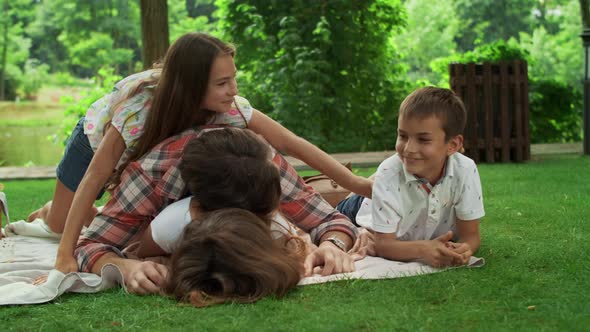 Family Lying on Blanket in Park. Parents Having Fun with Children in Forest