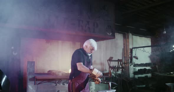Old Blacksmith with Grey Hair and Beard Beating with Hammer