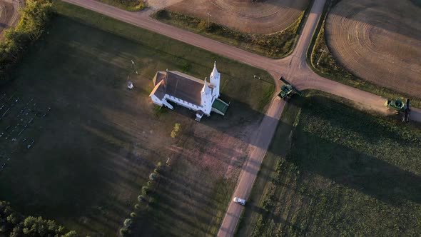 Aerial shot of roman catholic church in north American prairie during sunset. White building with bl