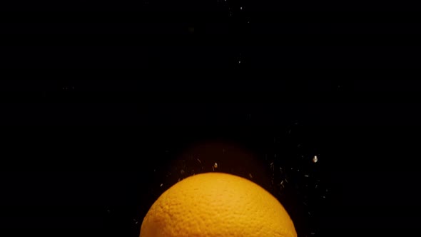 Closeup of Falling Ripe Orange Into the Sparkling Water on Black Background Making a Cocktail of