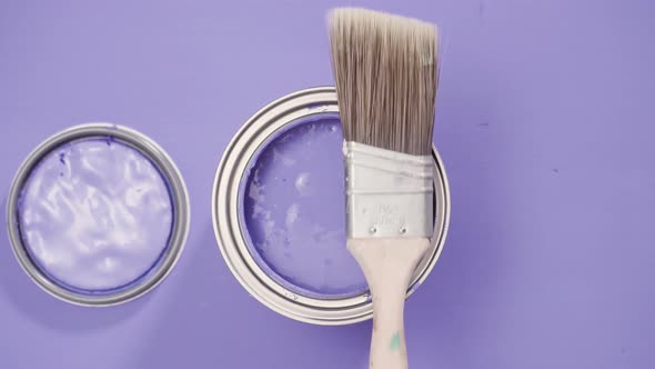 Opened metal paint can with purple paint and paint brush.