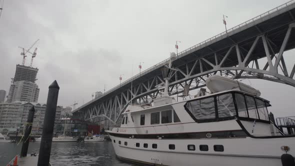 Yacht anchored in Granville island dock under bridge on cloudy day