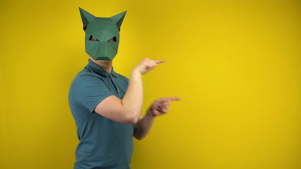 A Young Man in a Cardboard Jackal Mask Points To the Empty Space with His Index Fingers on a Yellow