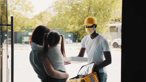 An AfricanAmerican Courier in Gloves and a Mask Delivers Food and Goods During a