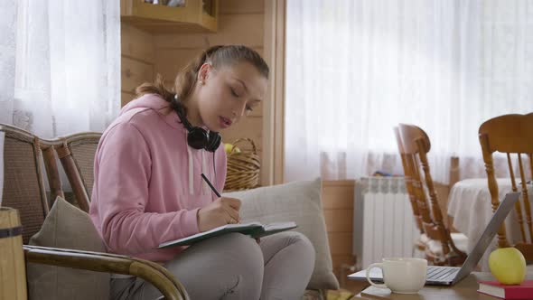 Young Caucasian Student Girl in Pink Hoodie Studying at Home During Quarantine.