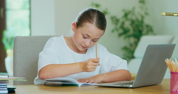 Cute Teen Girl at the Desk with Laptop Doing Homework Checking Tasks on Laptop Writing in Notebook