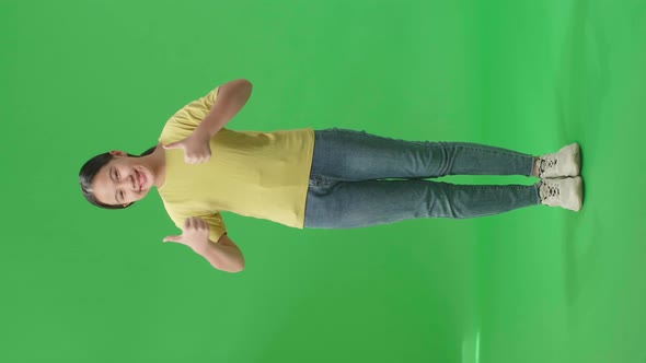 Full Body Of Happy Young Asian Kid Girl Showing Thumbs Up Gesture While Standing In The Green Screen