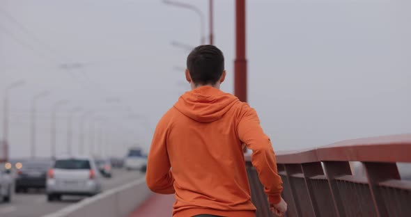 Man in Orange Hoodie Running on a Bridge Back View