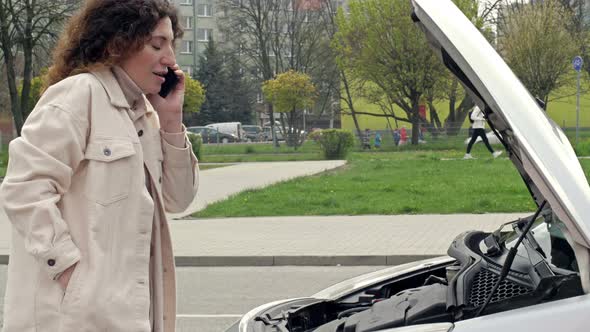 Middleaged Woman Driver Stands Near the Open Hood of Her Car