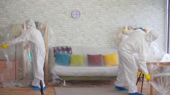 Workers in Protective Suits Cover the Furniture with Plastic Wrap