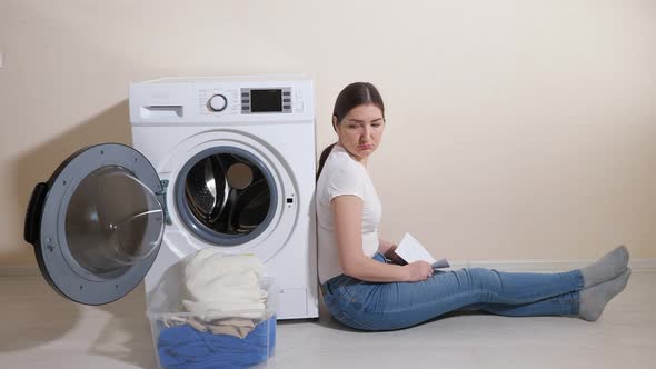 Upset Woman Sits on Floor Near Washing Machine in Room