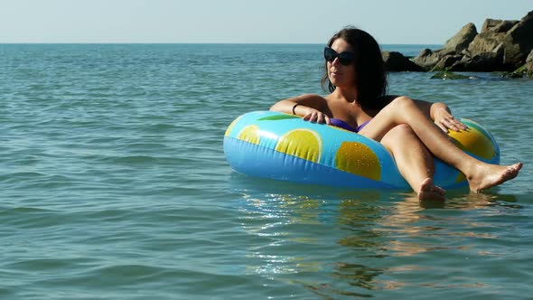 Young woman lying on an inflatable mattress with lemons, floating and relaxing in the sea.