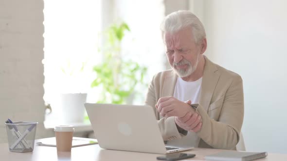 Old Man Having Wrist Pain While Using Laptop in Office