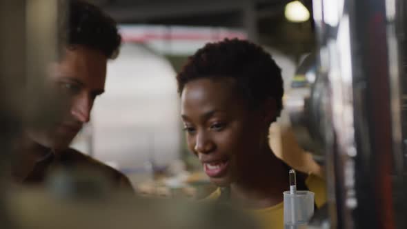 Diverse male and female colleague at gin distillery inspecting equipment and discussing