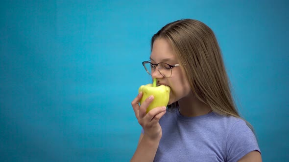 Teenage Girl with Braces on Her Teeth Eats Bell Pepper on a Blue Background. A Girl with Colored