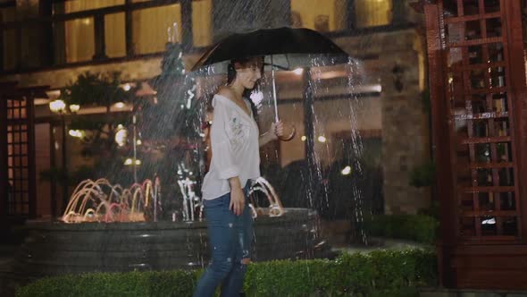 Stylish Wet Girl Walks with Umbrella Under Night Rain on Street