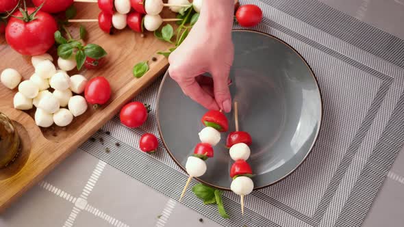 Putting Caprese Canapes with Cherry Tomatoes and Mozzarella Cheese Balls on a Plate