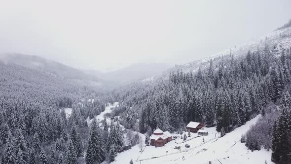 Flight Over Forest and a Village in a Mountain Valley in Winter