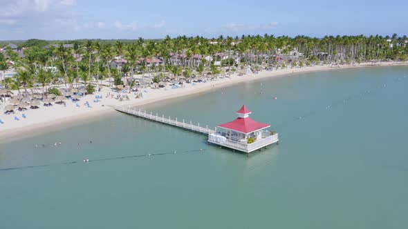 Aerial forward flight over jetty along sandy beach with sunshades and tropical palm trees - BAHIA PR