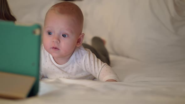 Cute Baby Girl Lying on a Bed and Watching on Tablet Screen