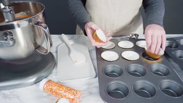 Scooping pumpkin spice cupcake batter with batter scoop into a cupcake pan with liners.