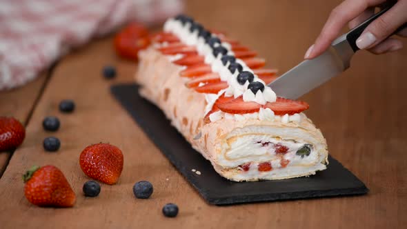 Close up, young girl is cutting meringue roulade with berries and mascarpone