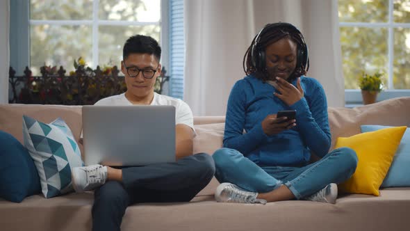 Happy Multiracial Couple with Modern Gadgets Networking or Messaging at Home