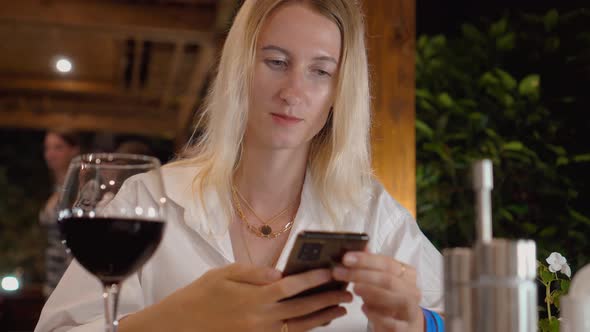 a woman sits in restaurant in white shirt and looks into smartphone
