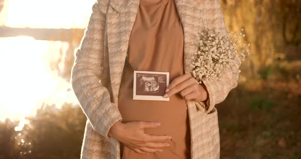 Pregnant Blonde Woman with a Bouquet on the Shore of the Pond