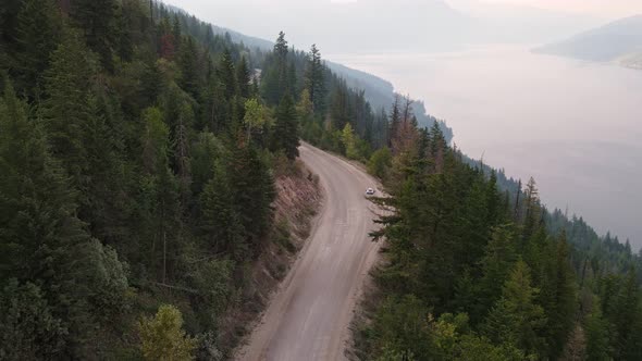 Silver van driving along a dusty forest service road in Canada during wildfire season with Adams Lak