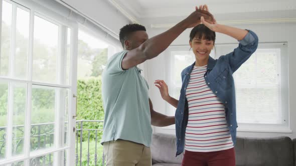 Happy diverse couple holding hands and dancing in living room