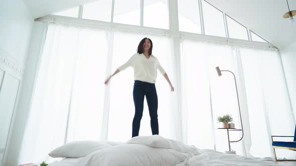slow motion of exited asian woman jump over white bed in bedroom with energy and happiness success